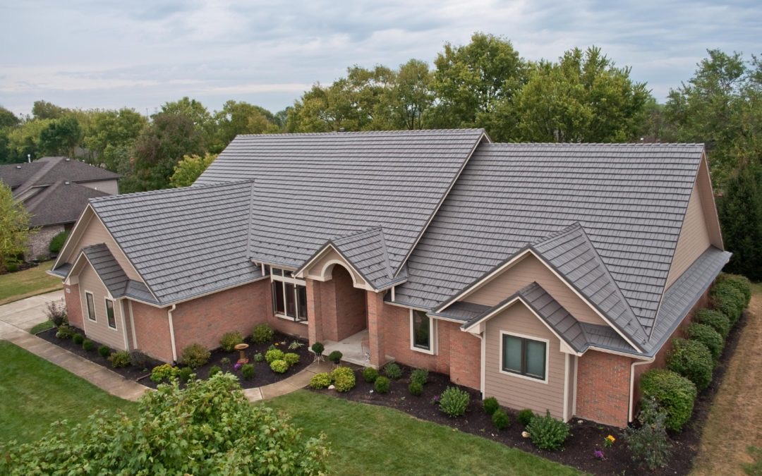 Drone view of suburban home with dark grey architectural shingle roof, red brick and tan siding facade