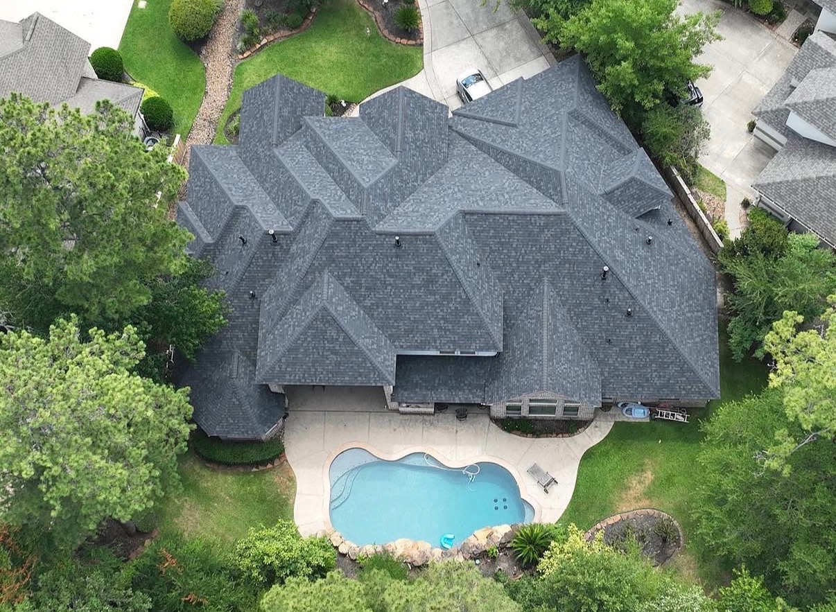 Aerial view of completed dark grey architectural asphalt shingle roof replacement on a large residential property with swimming pool
