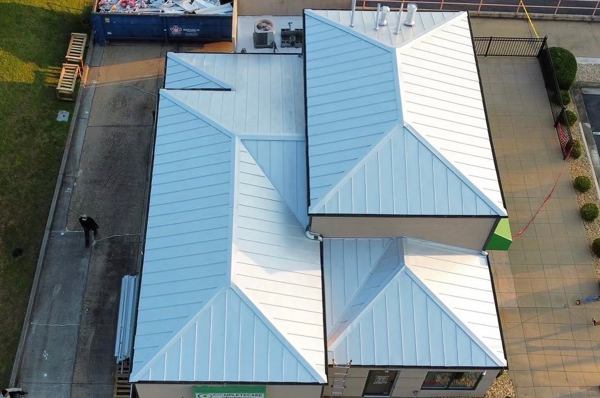 Aerial view of commercial building with newly installed light-colored standing seam metal roof replacement