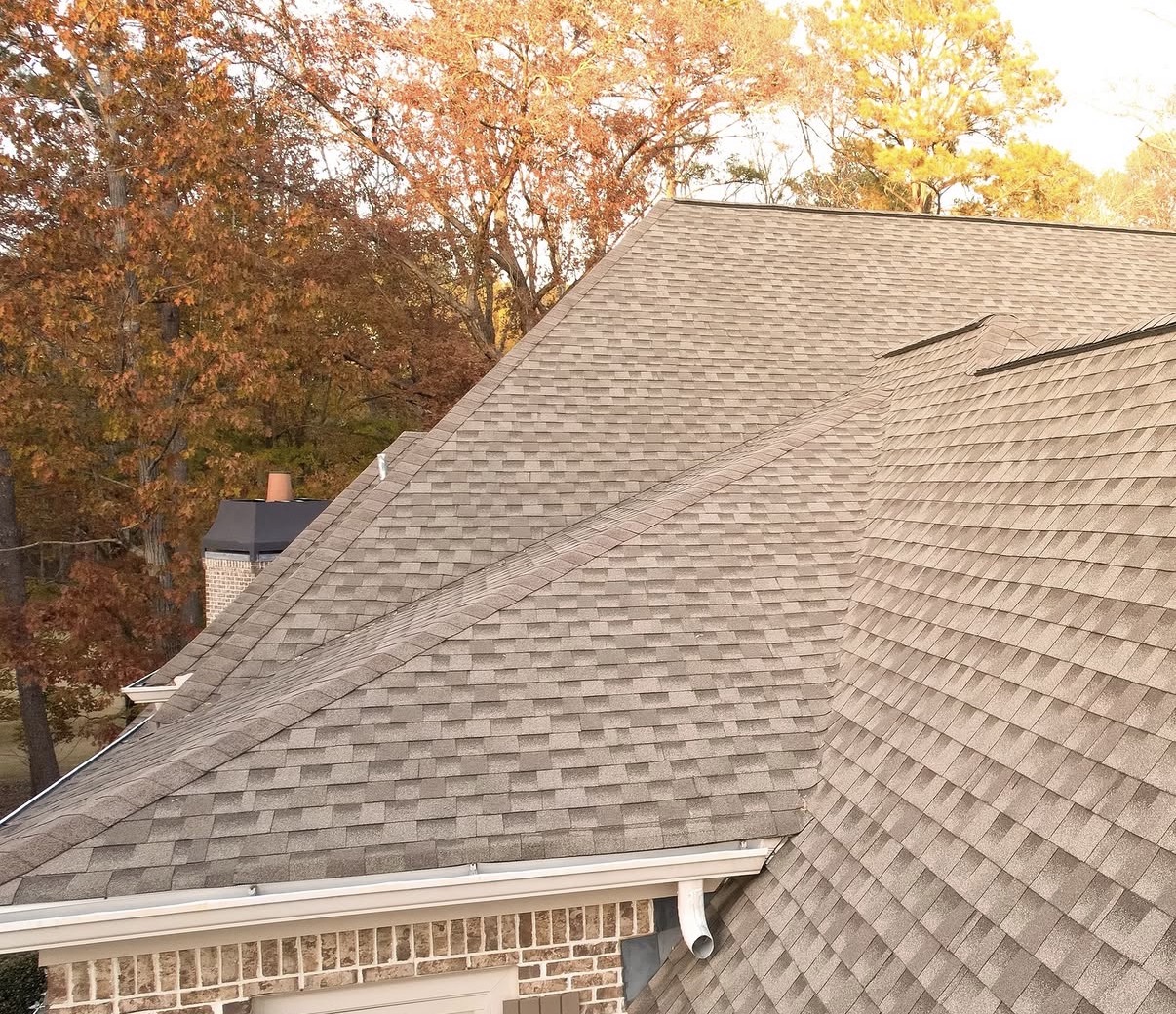 High-angle view of multi-pitched residential roof with new grey architectural asphalt shingles and white gutter system