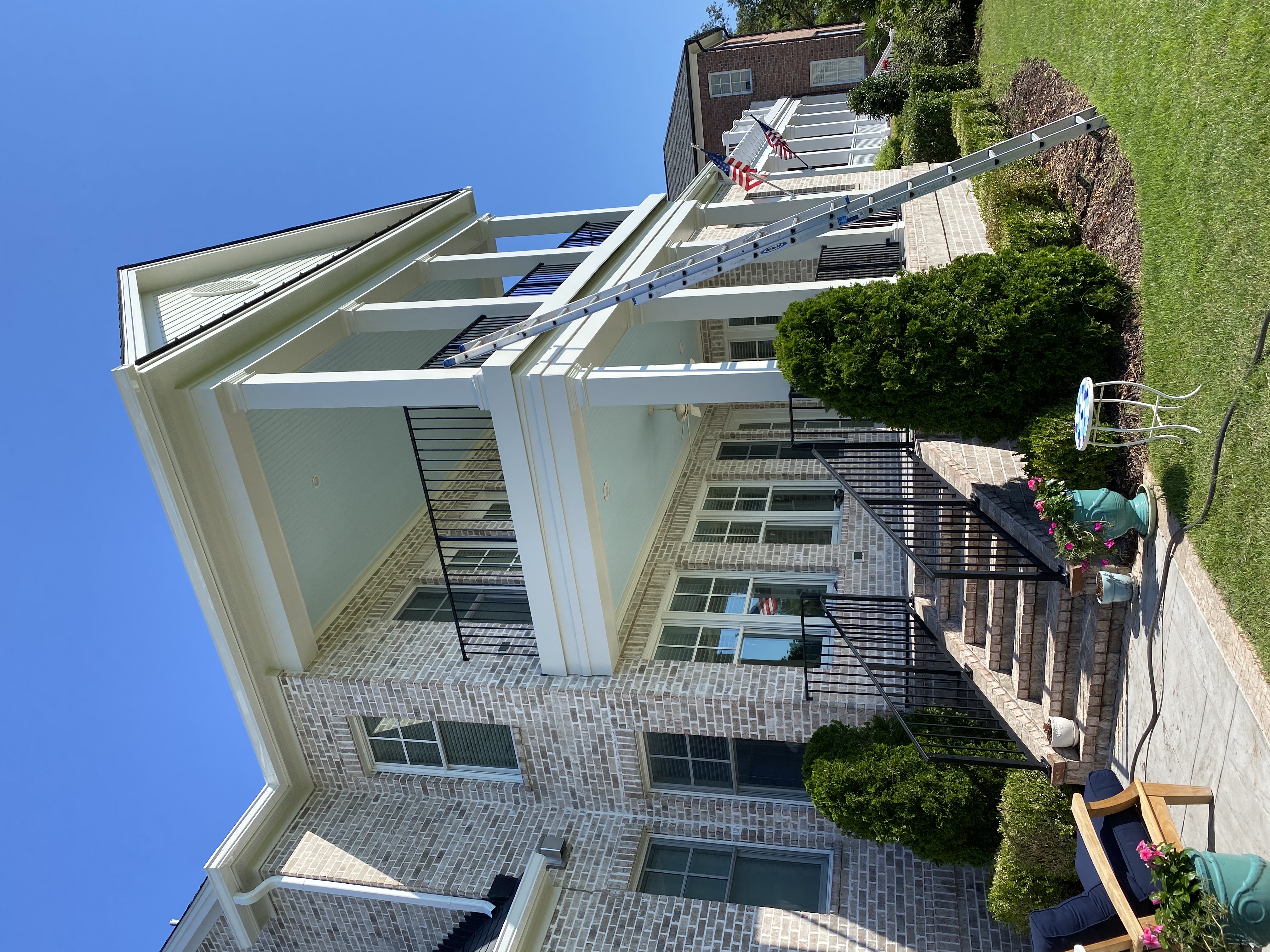 Multi-story white brick home with multi-tiered porch, white columns, black railings, and light blue porch ceilings during exterior restoration