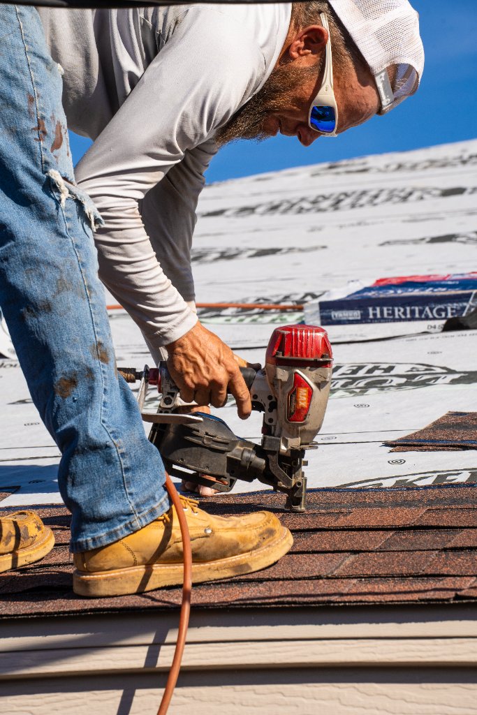Roofer using nail gun on shingles