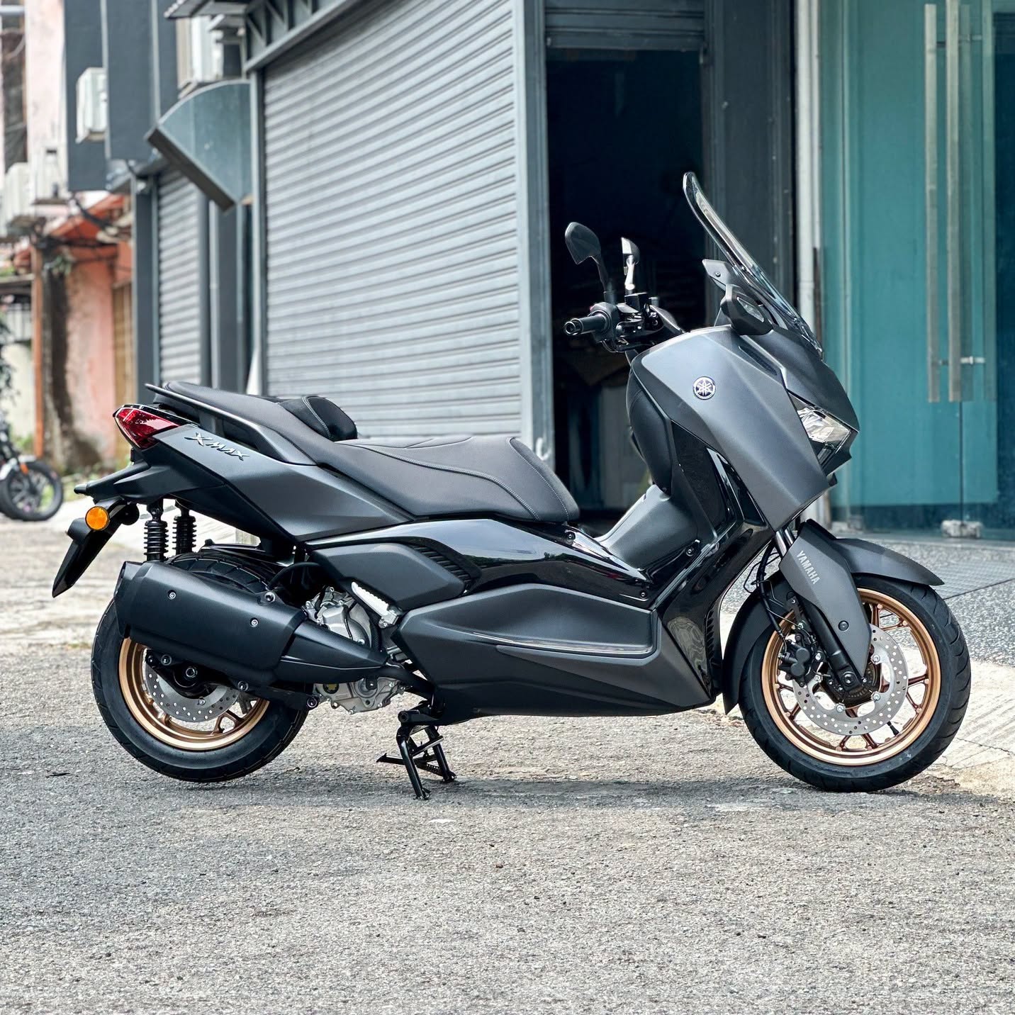 Yamaha XMAX 300 side profile with matte grey bodywork and bronze-gold rims