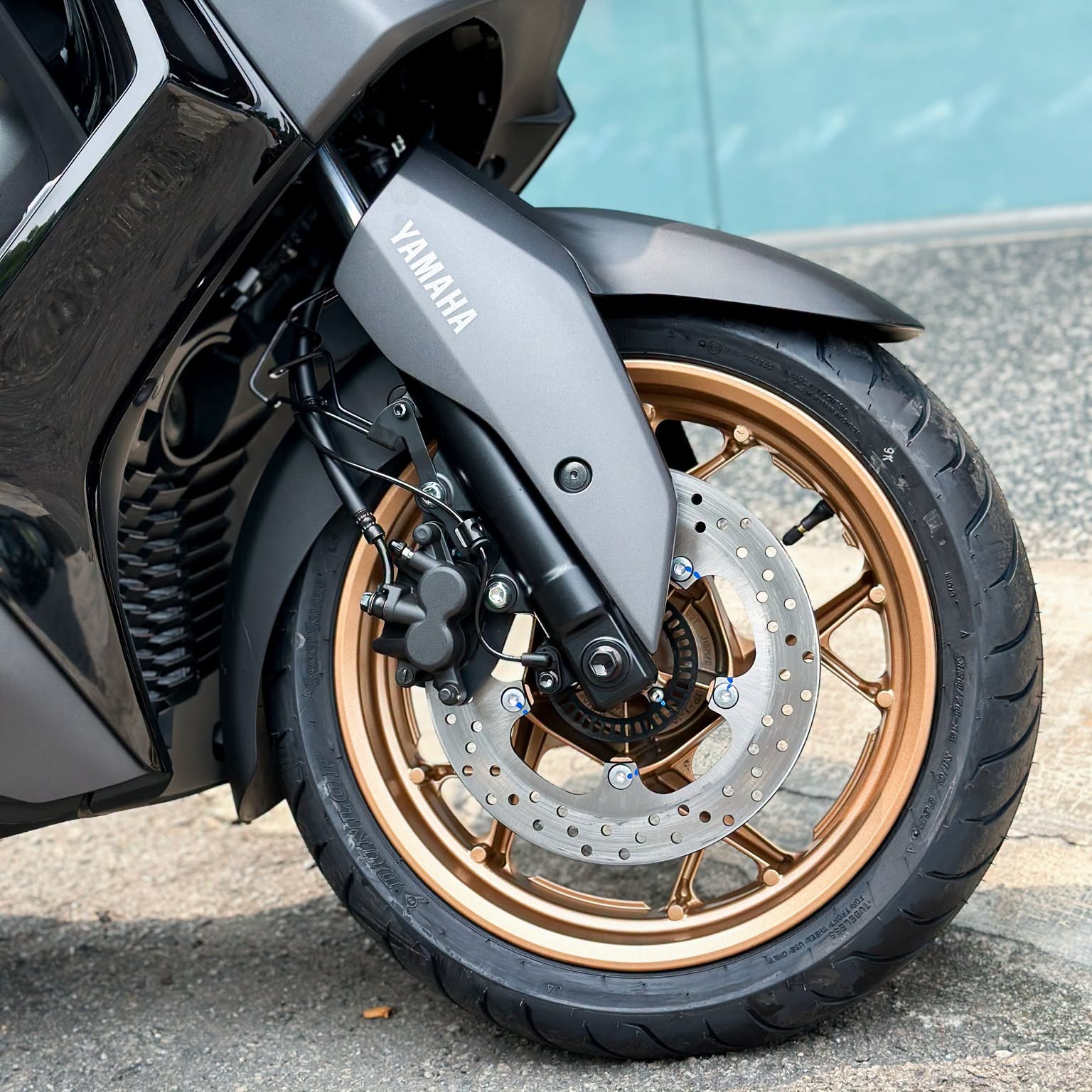 Yamaha XMAX 300 front wheel detail showing bronze-gold rim, drilled disc brake and black caliper