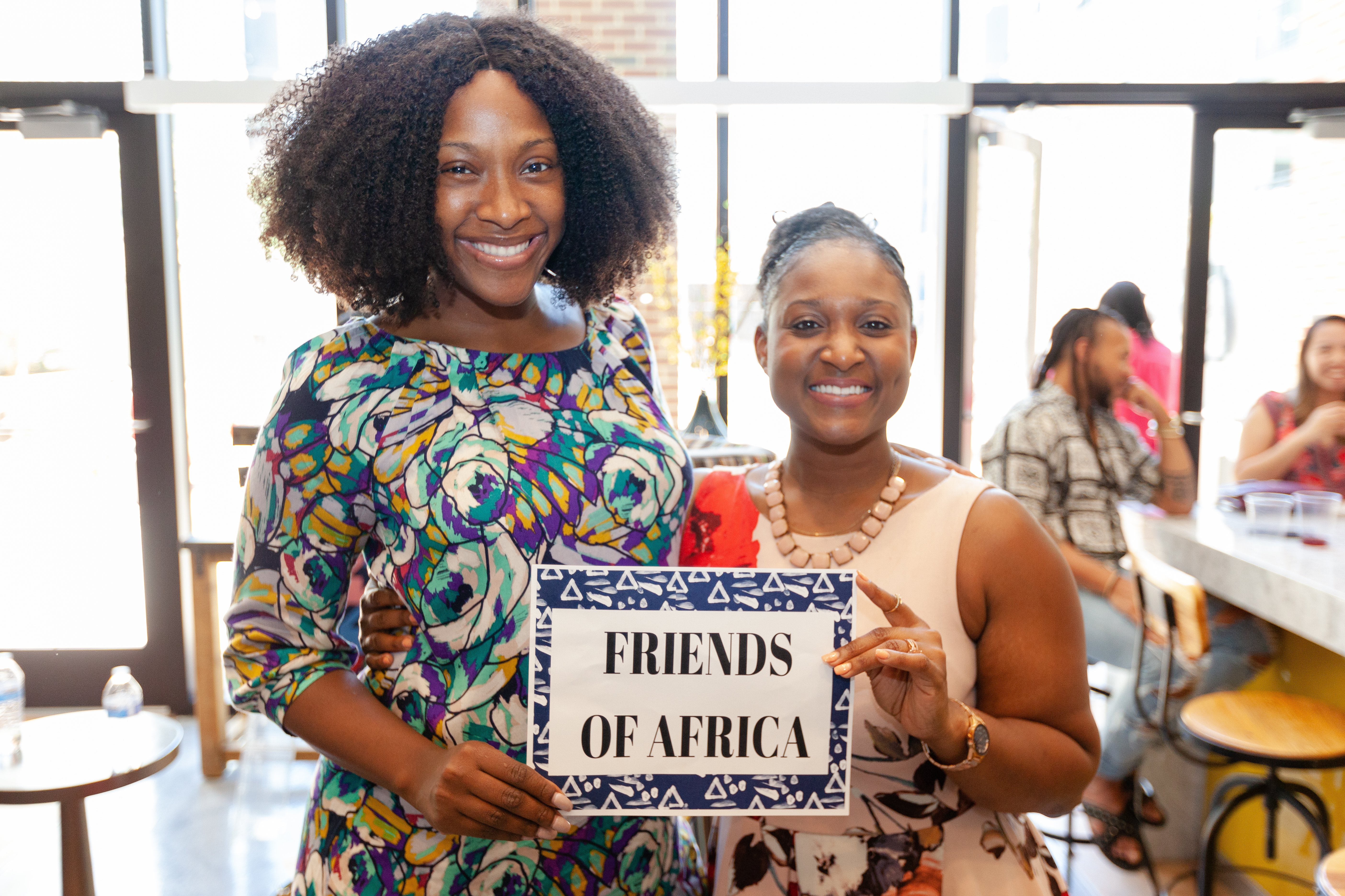 Queen Mercy holding a Friends of Africa sign alongside a sister in community