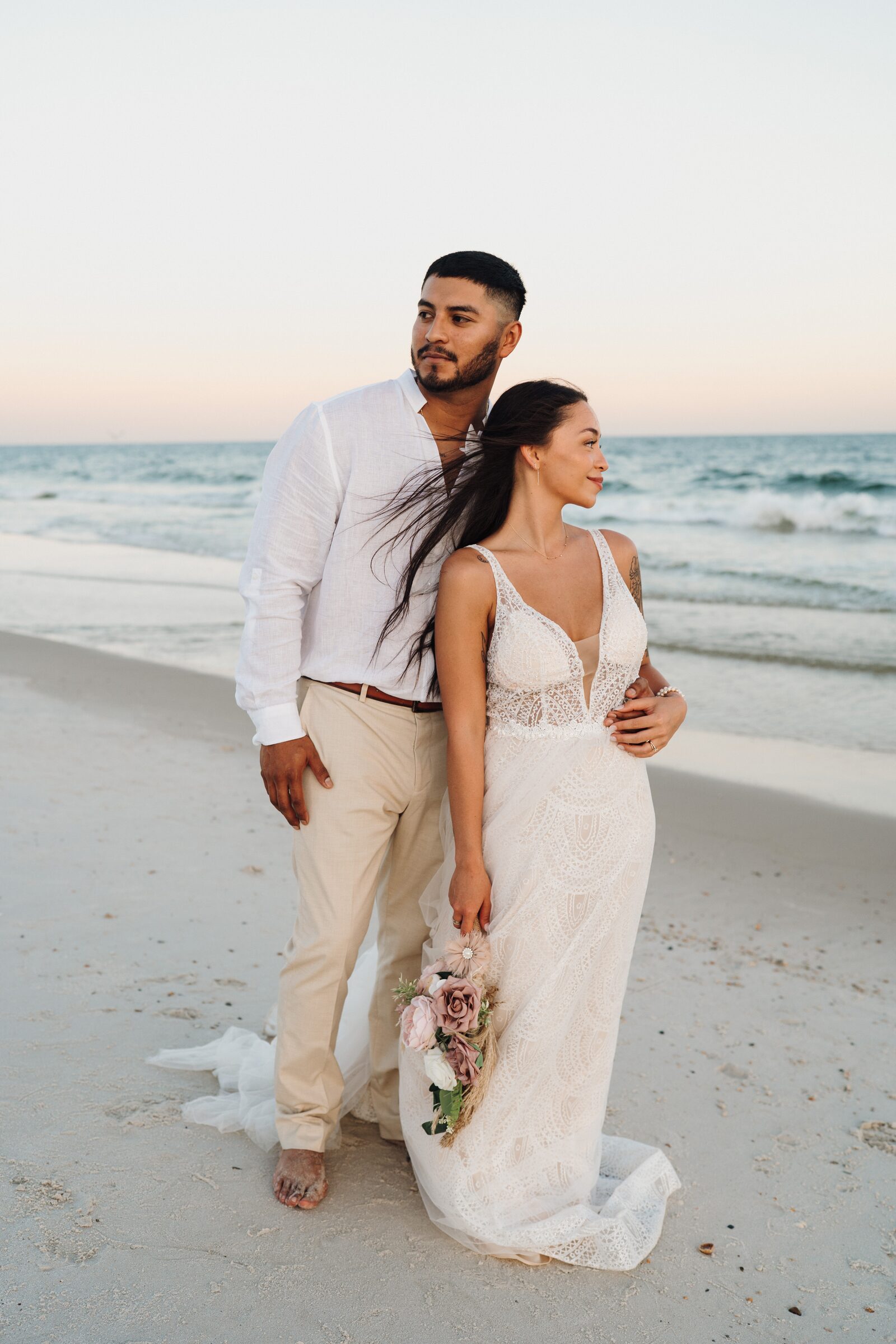 Bride and groom facing each other on the beach at sunset