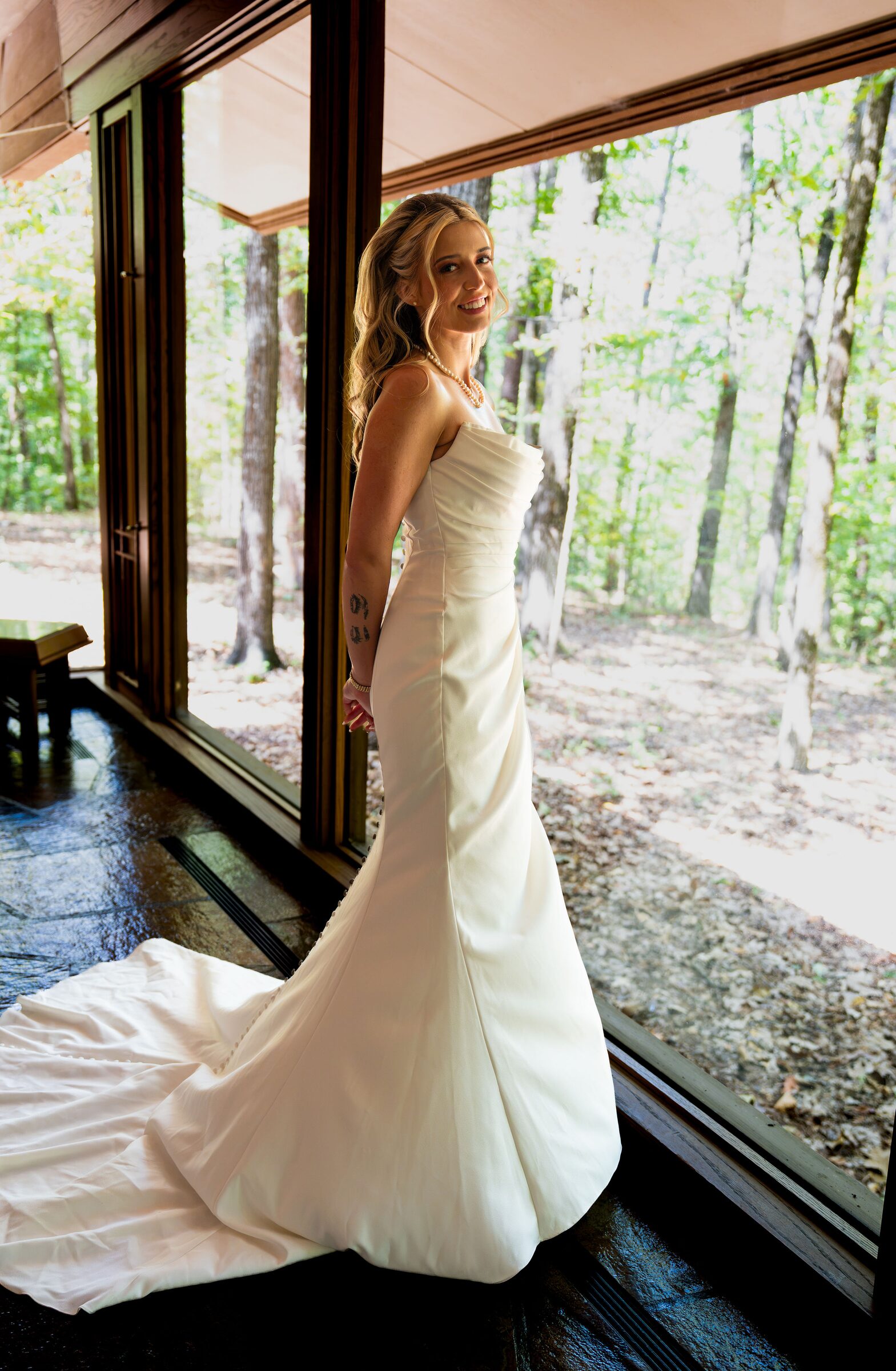 Bride in a white gown with a long train standing inside a glass walled chapel