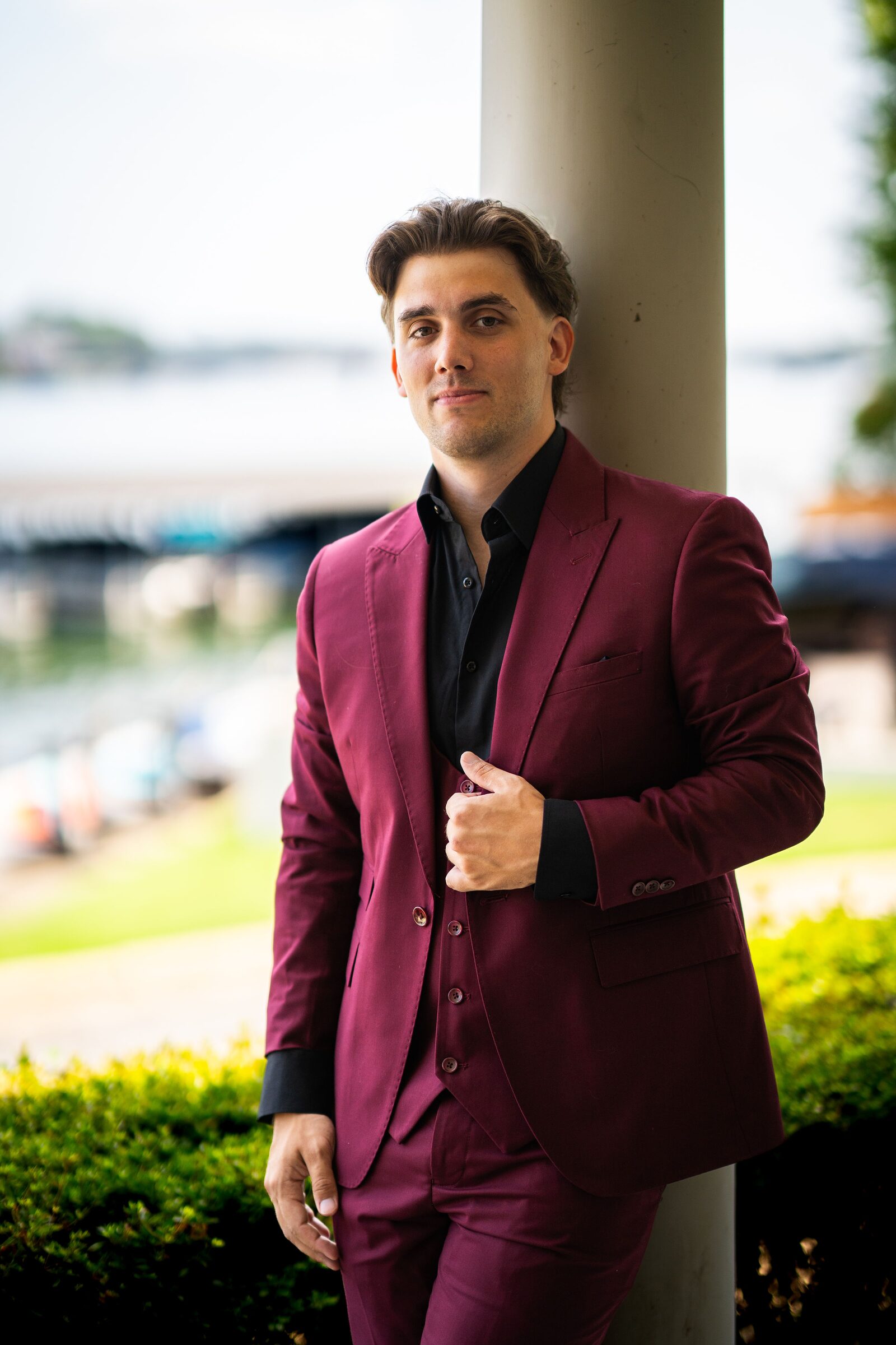 Groom in a burgundy suit leaning against a pillar at Garvan Woodland Gardens, Hot Springs, Arkansas