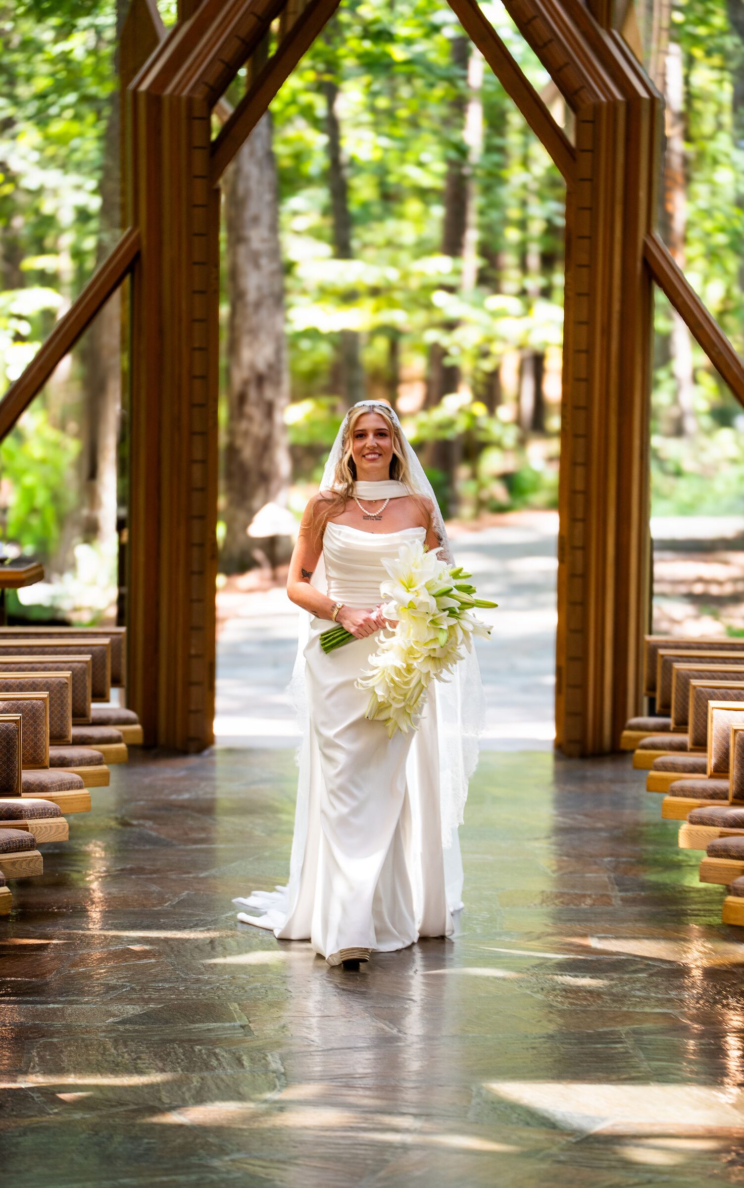 Bride carrying a cascade of white lilies down the stone aisle at Garvan Woodland Gardens, Hot Springs, Arkansas
