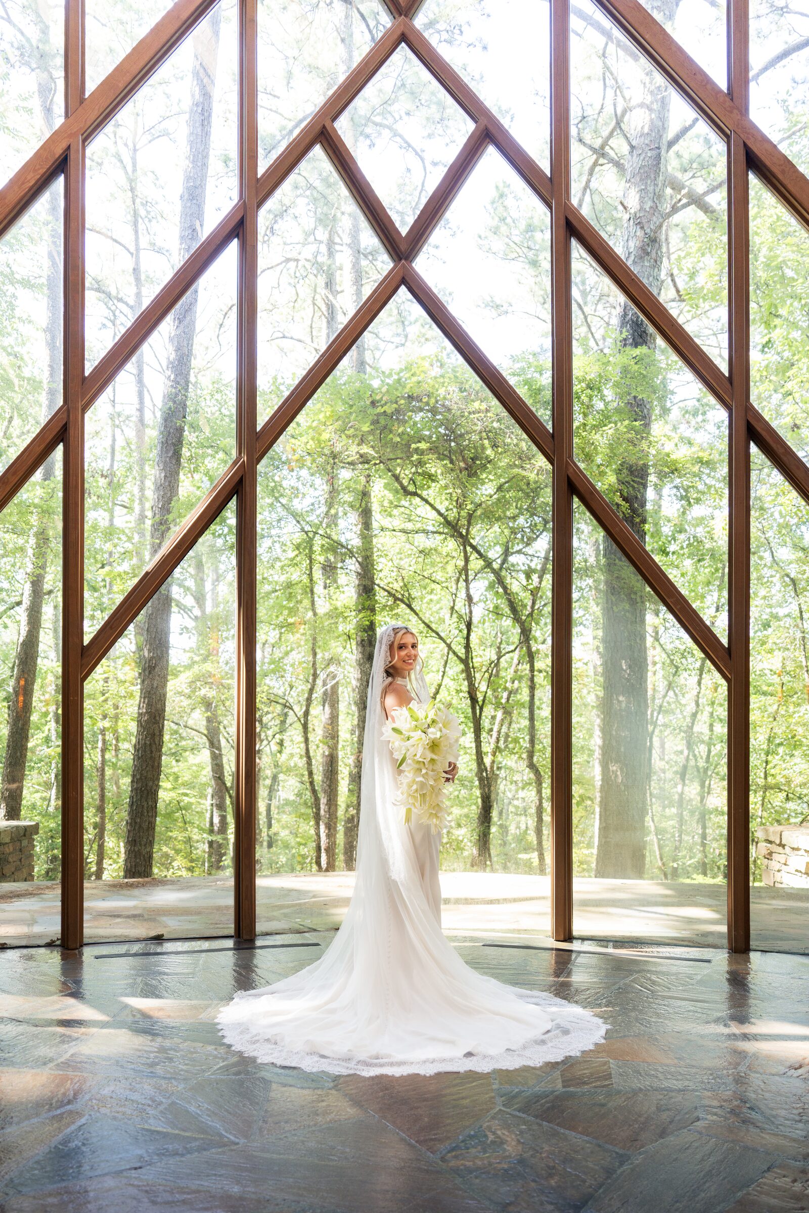 Bride holding a cascade of lilies and looking back over her shoulder inside the chapel at Garvan Woodland Gardens, Hot Springs, Arkansas