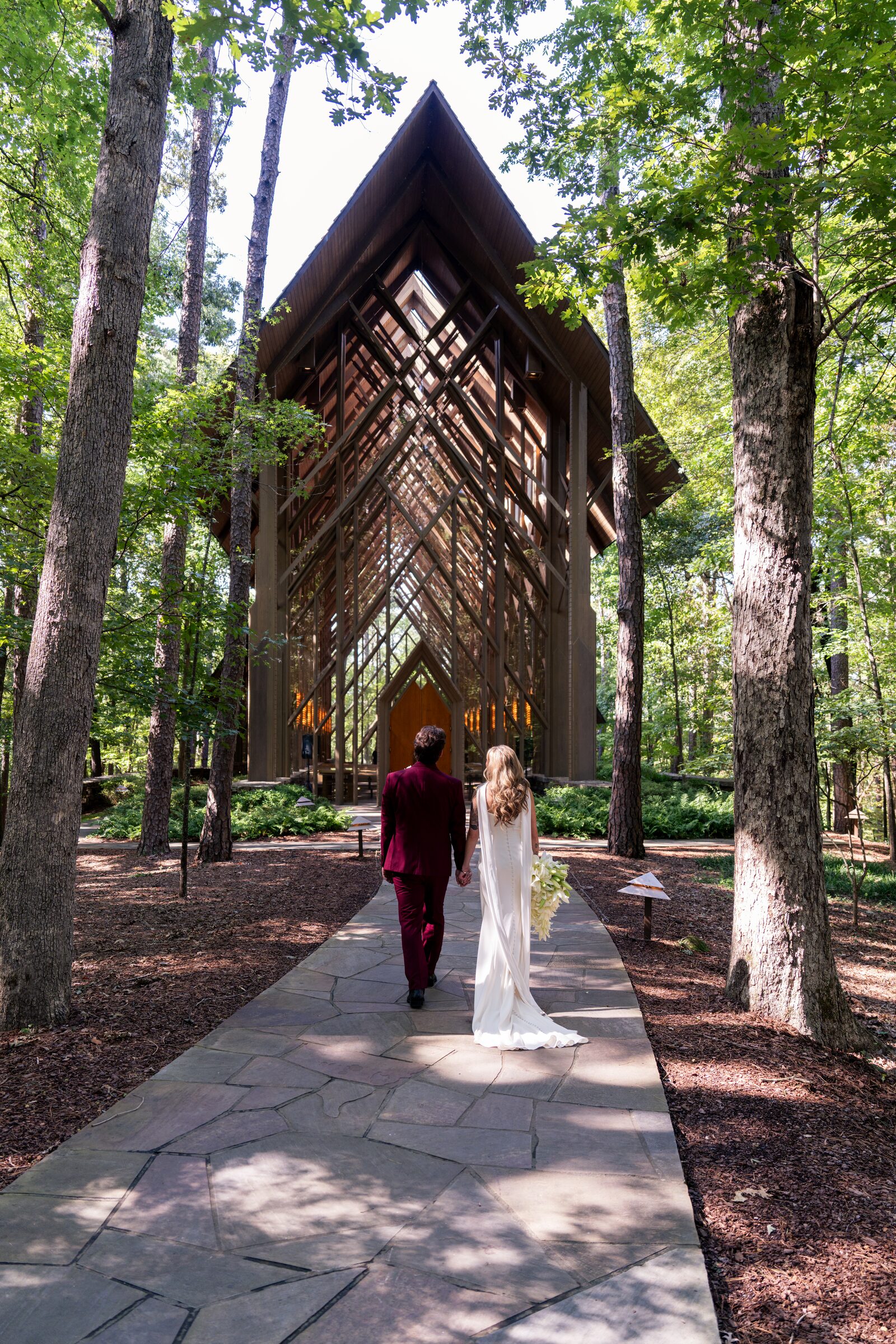 Bride and groom walking hand in hand along a stone path toward the chapel