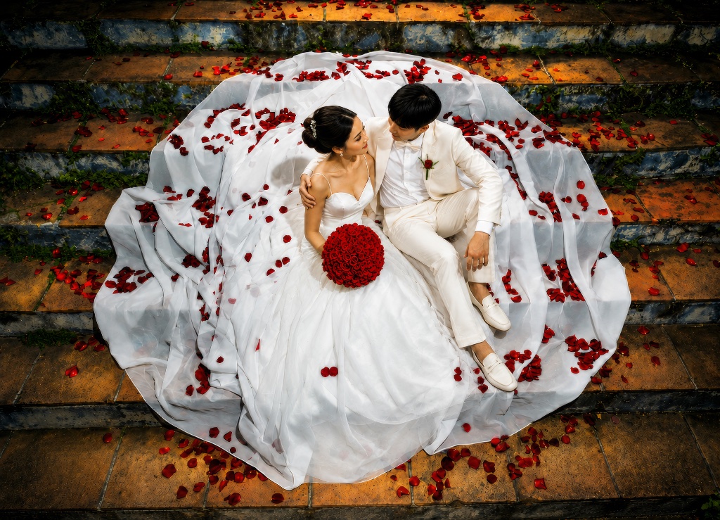 Bride and groom on stone stairs surrounded by red rose petals