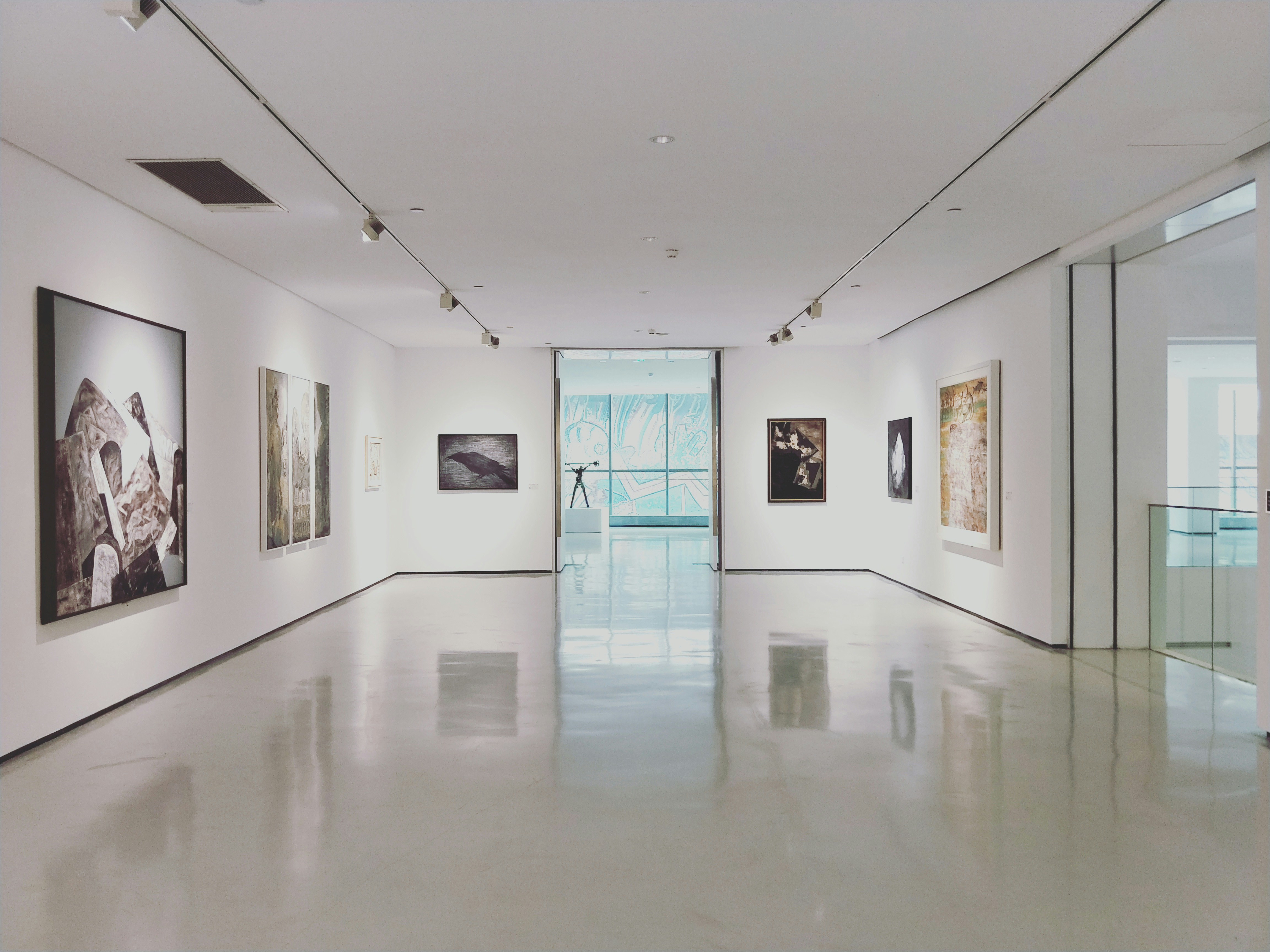Dimly lit gallery corridor with individually spotlit contemporary works.