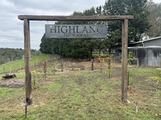Custom laser cut "Highland Hideaway" metal sign hanging from a wooden post frame outdoors