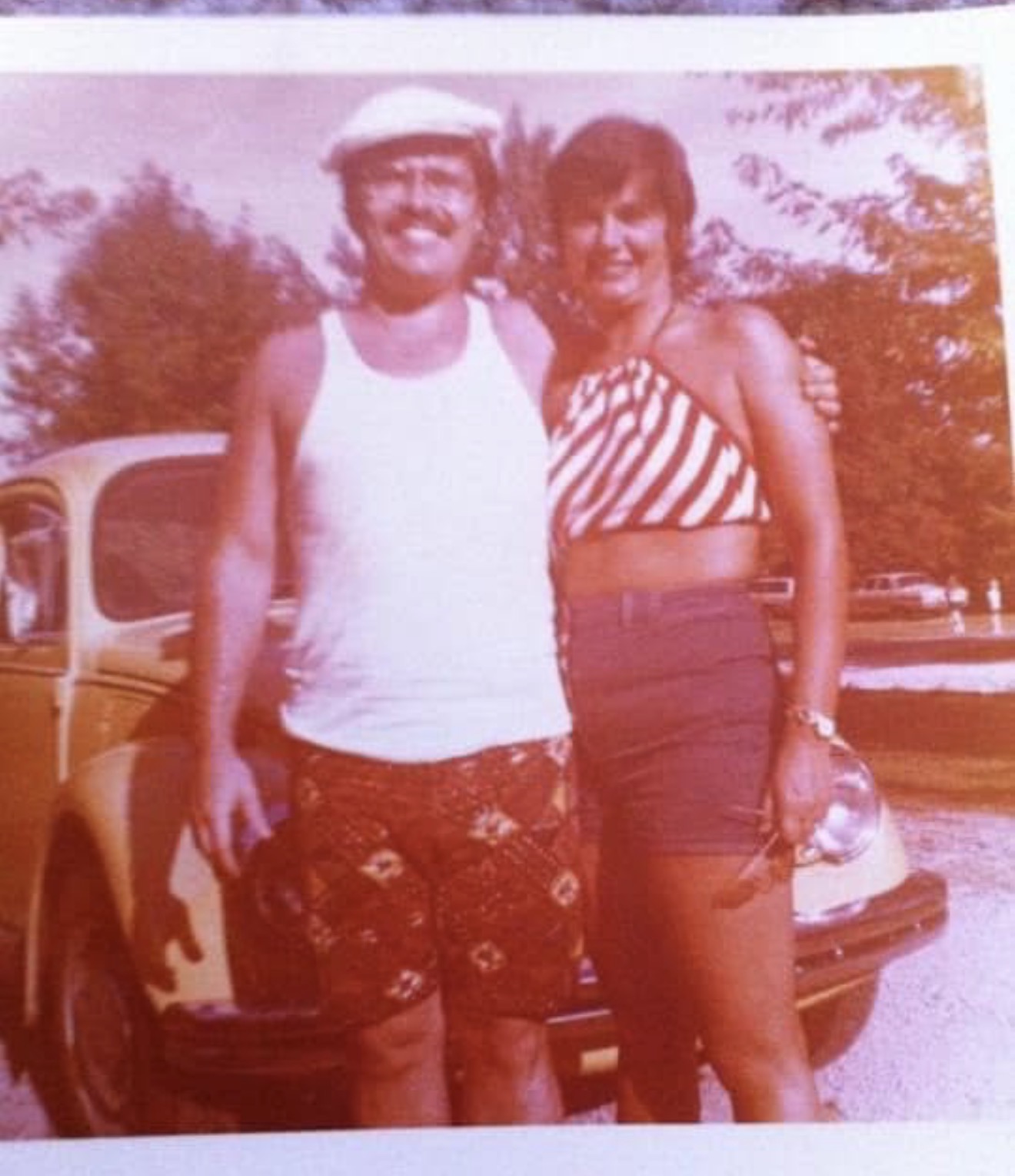 A couple standing in front of a Volkswagen Beetle, faded snapshot