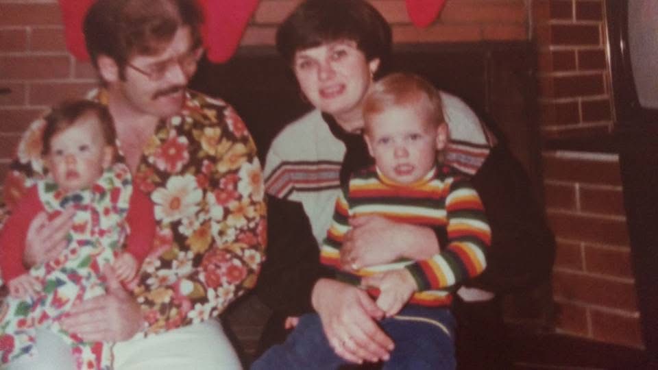 A 1970s family by the fireplace, two babies on laps