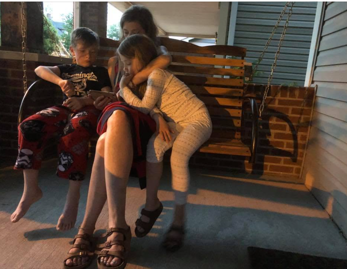 Three children resting together on a front porch swing in late afternoon light.