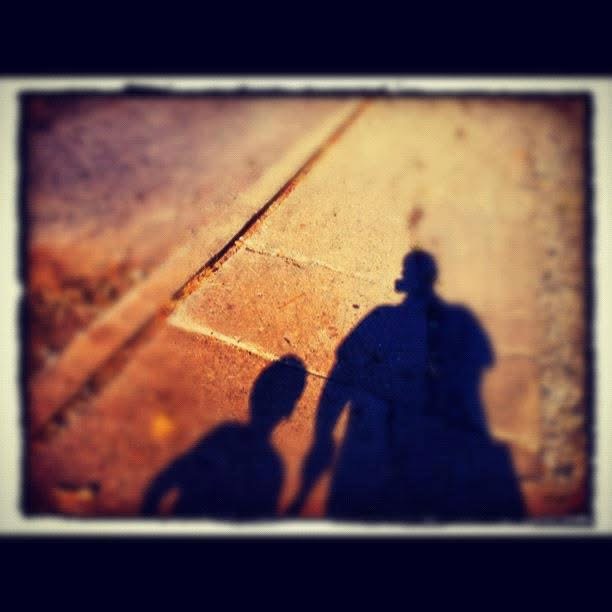 Shadows of an adult and a child holding hands, cast on a sunlit sidewalk