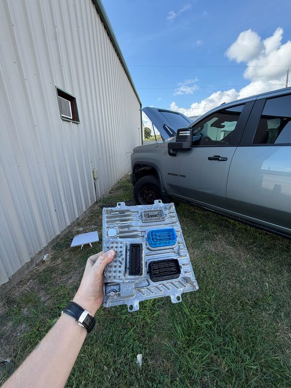 ECM in hand next to a Chevrolet 2500HD