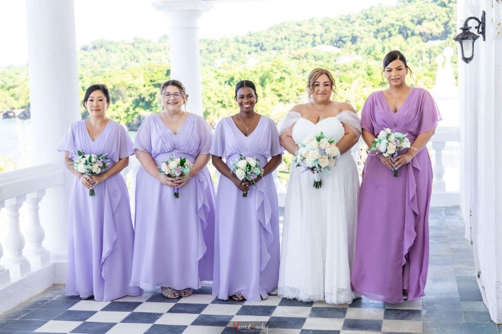Bride with four bridesmaids in lavender gowns on castle veranda with ocean backdrop