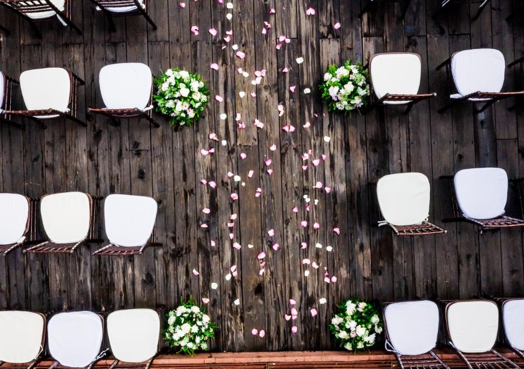 Aerial drone top-down shot of petal aisle with chiavari chairs and white floral clusters on dark wood deck