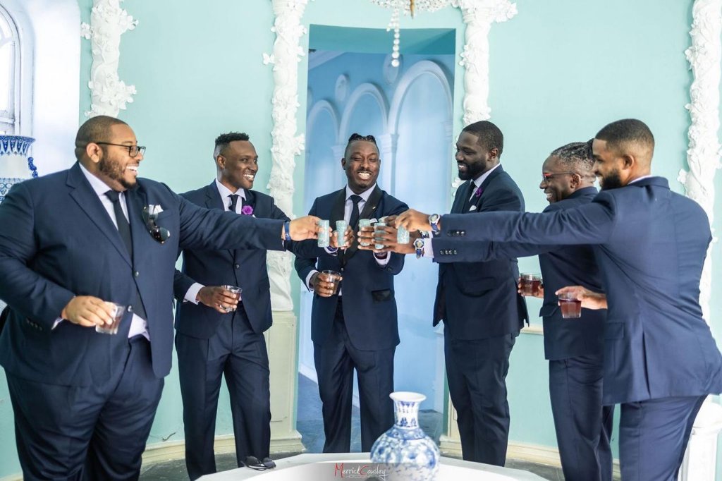 Groomsmen in navy suits toasting in the ornate blue room at Trident Castle