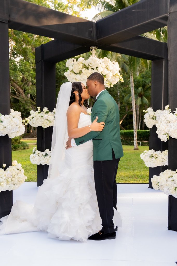 First kiss close-up framed by black altar structure with white hydrangeas all around