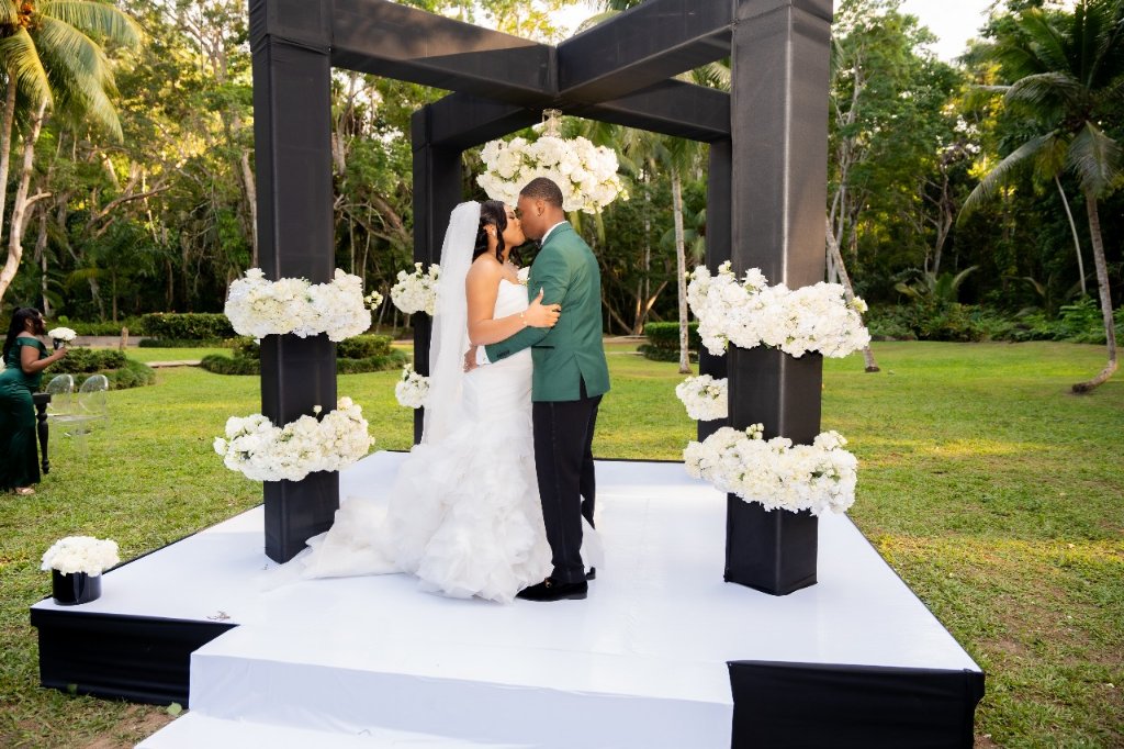 First kiss wide shot on black geometric altar stage with white hydrangeas, tropical garden