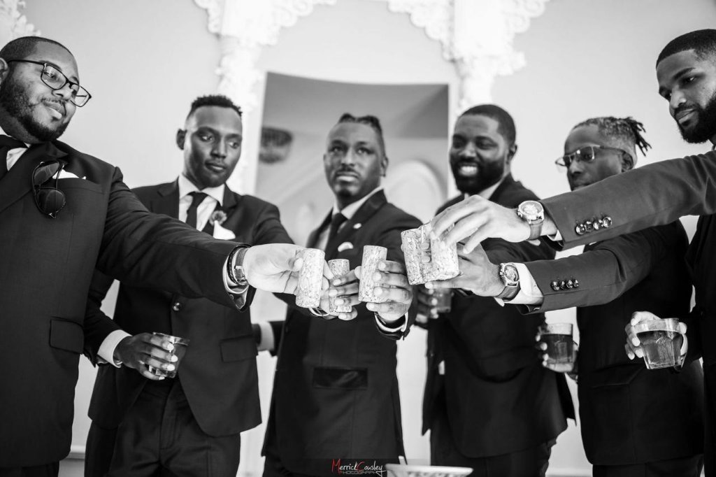 Groomsmen toasting in black and white — close-up of raised rum shots