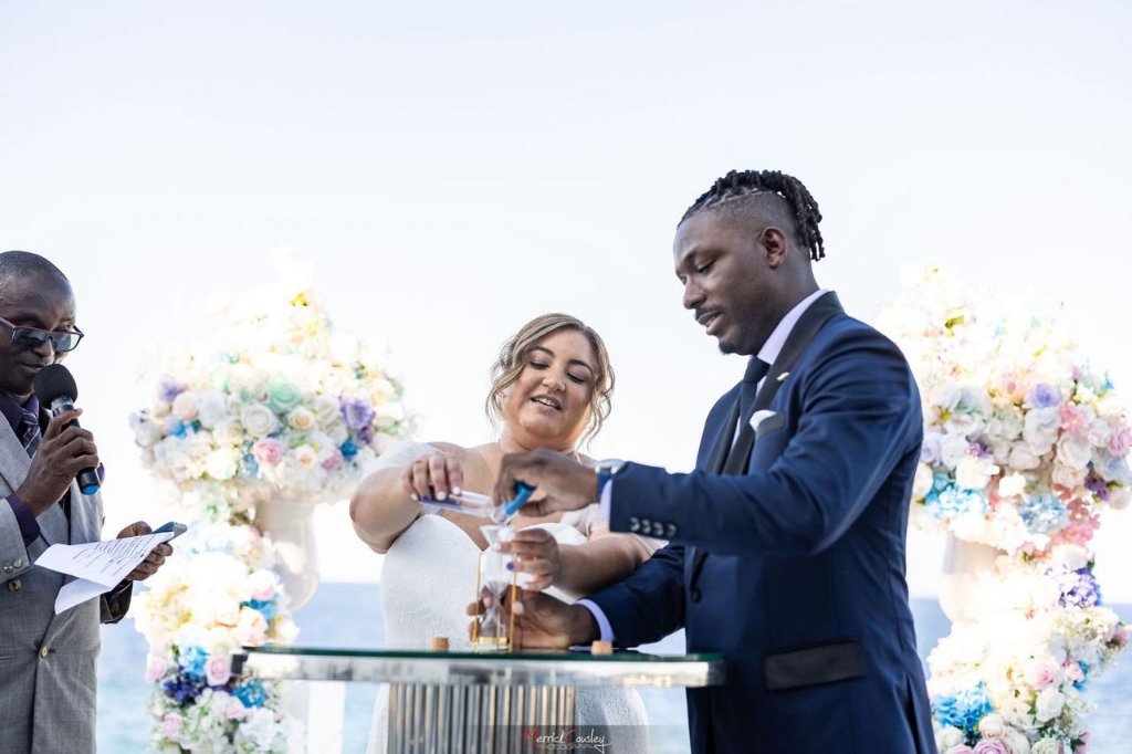 Unity sand ceremony with officiant and pastel floral pillars at oceanfront