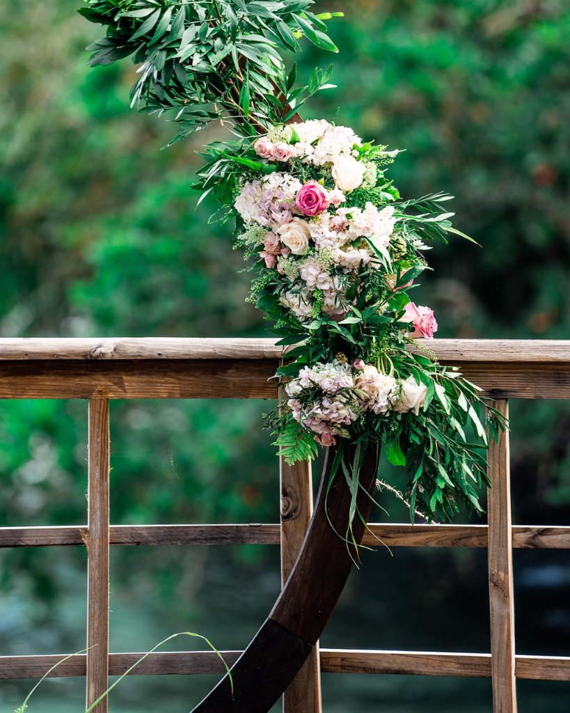 Close-up of cascading floral garland on circular arch — blush roses, hydrangeas and tropical greenery spilling over the railing