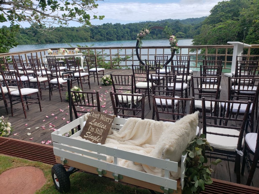 Ceremony deck with 'Don't Worry Ladies, I'm Still Single!' wagon in foreground, petal aisle and circular arch with San San Bay behind