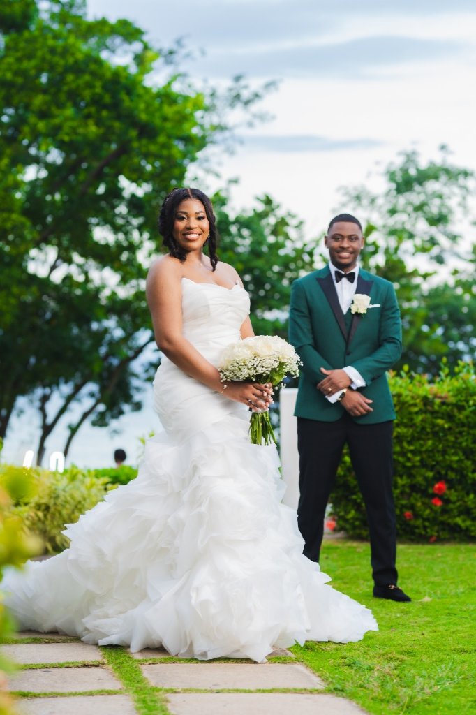 Couple portrait on lawn, groom in emerald tux, bride in ruffled gown, tropical sky behind