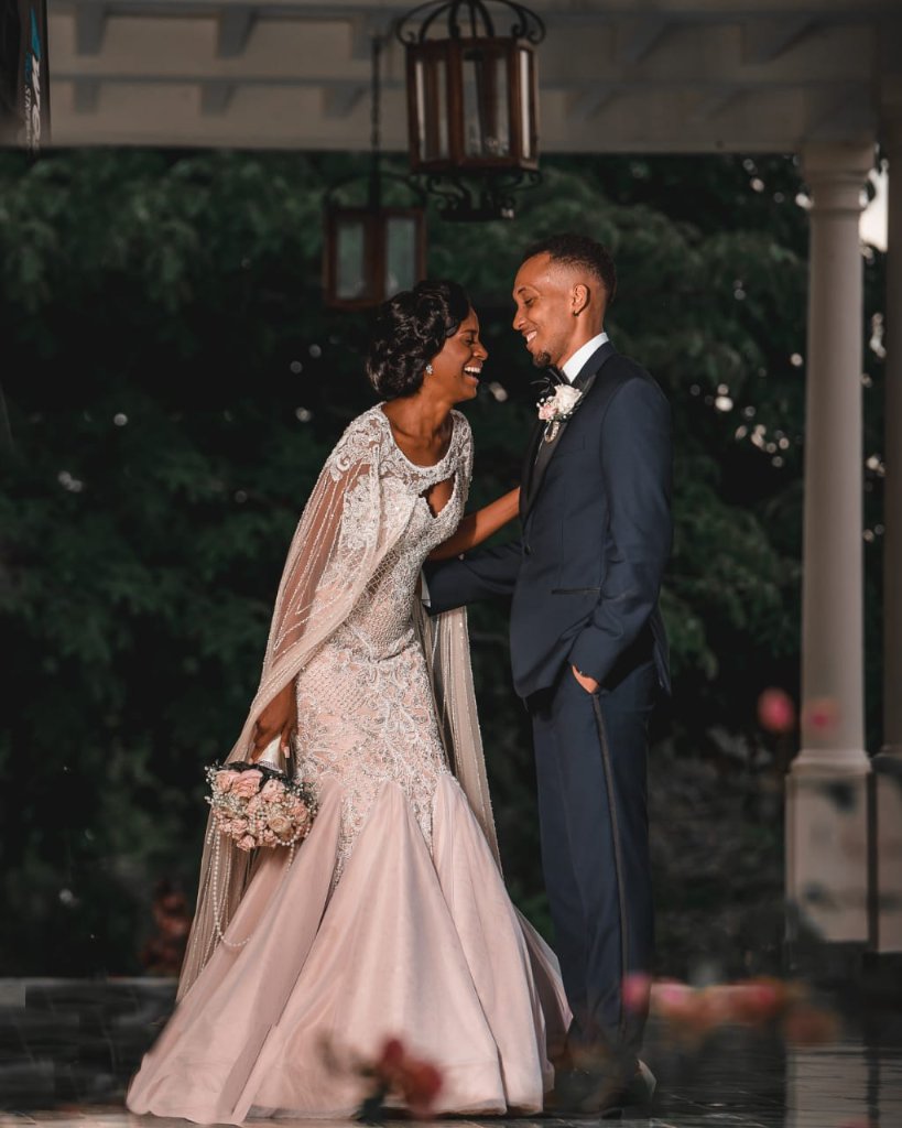 Couple laughing together under estate portico, lantern above, rose petals scattered on the marble floor