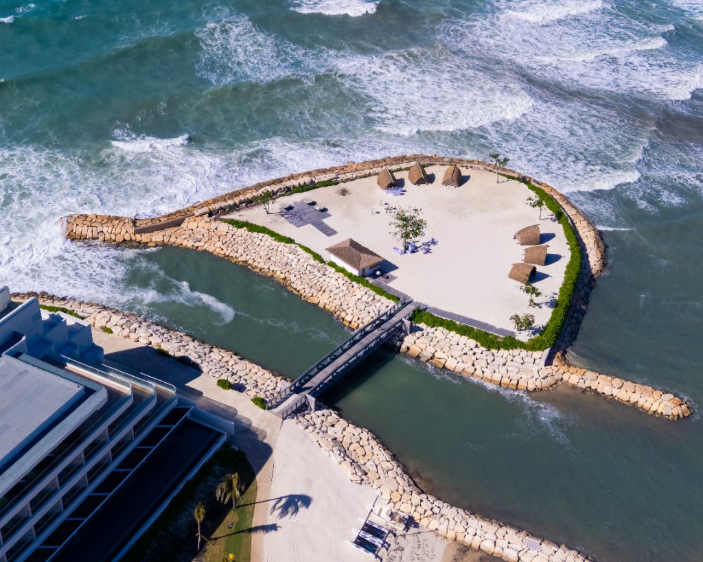 Aerial drone shot of Princess Resorts private island ceremony location — teardrop-shaped islet surrounded by turquoise Caribbean Sea with ceremony arch visible
