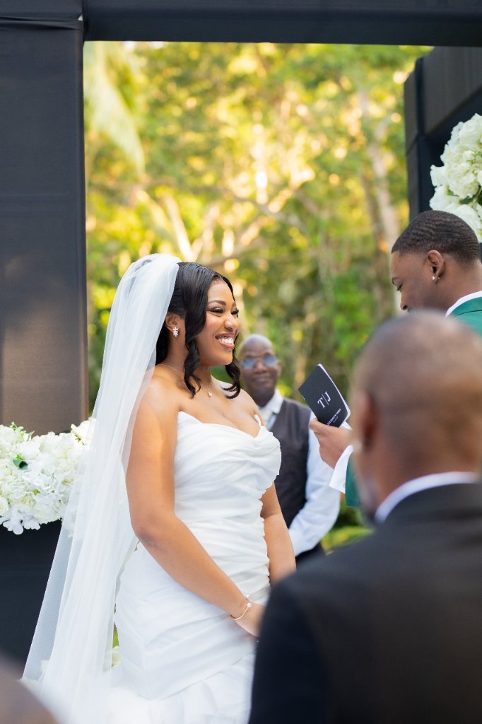 Bride beaming with joy at altar as groom reads vows from personalised black booklet