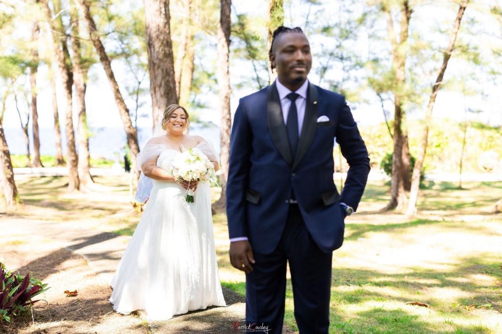 Bride approaching groom from behind through sunlit pine grove for first look