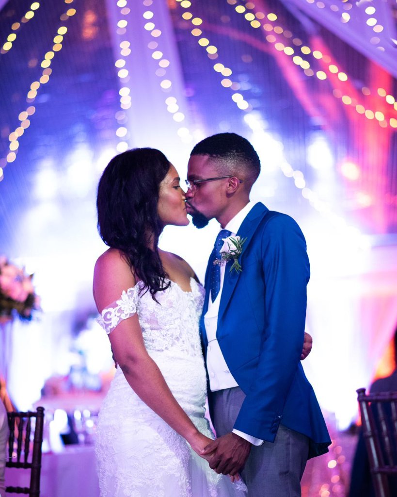 Couple kissing under fairy lights and purple uplighting inside the reception marquee