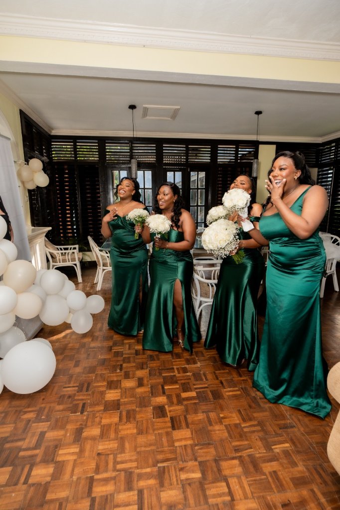 Four bridesmaids in emerald satin gowns reacting with joy and surprise at first look
