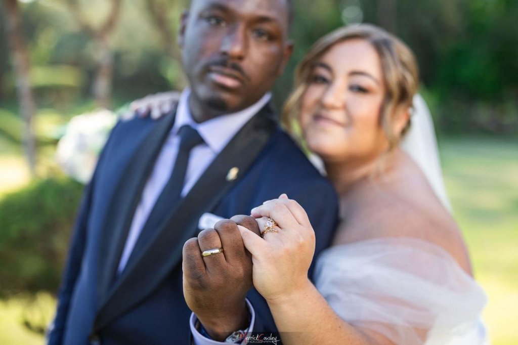 Close-up of couple holding hands showing both wedding rings in garden setting