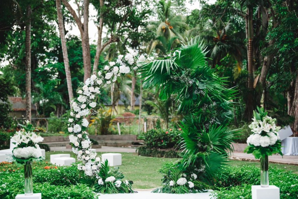 Floral arch and white runway stage set in lush tropical garden