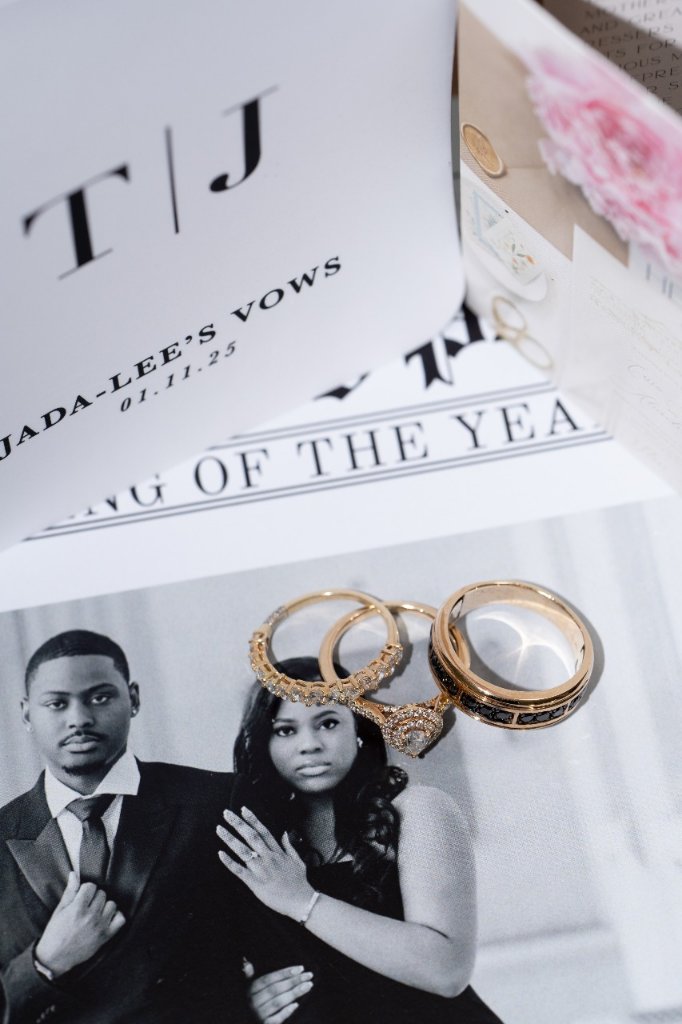 Flat lay of T|J vow books and wedding rings resting on engagement photo with pink florals