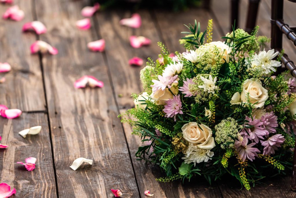 Aisle floral arrangement of cream roses, lavender daisies and greenery resting on petal-covered dark wood planks