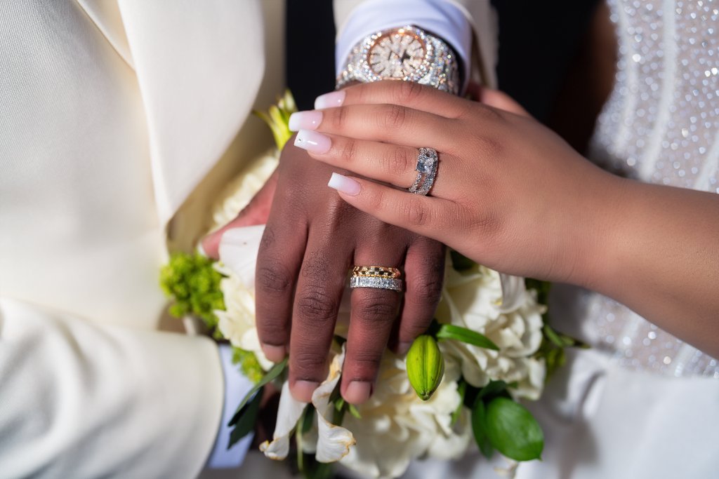 Couple posing together on resort boardwalk at golden hour, bride in beaded ball gown holding white bouquet, groom in white tuxedo jacket