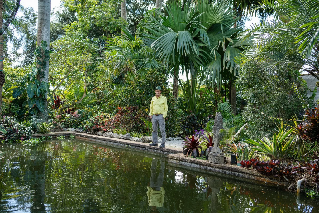 Jesse Durko standing by a tropical garden pond with a stone sculpture