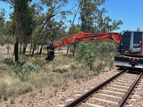 Grapple-equipped excavator clearing corridor vegetation