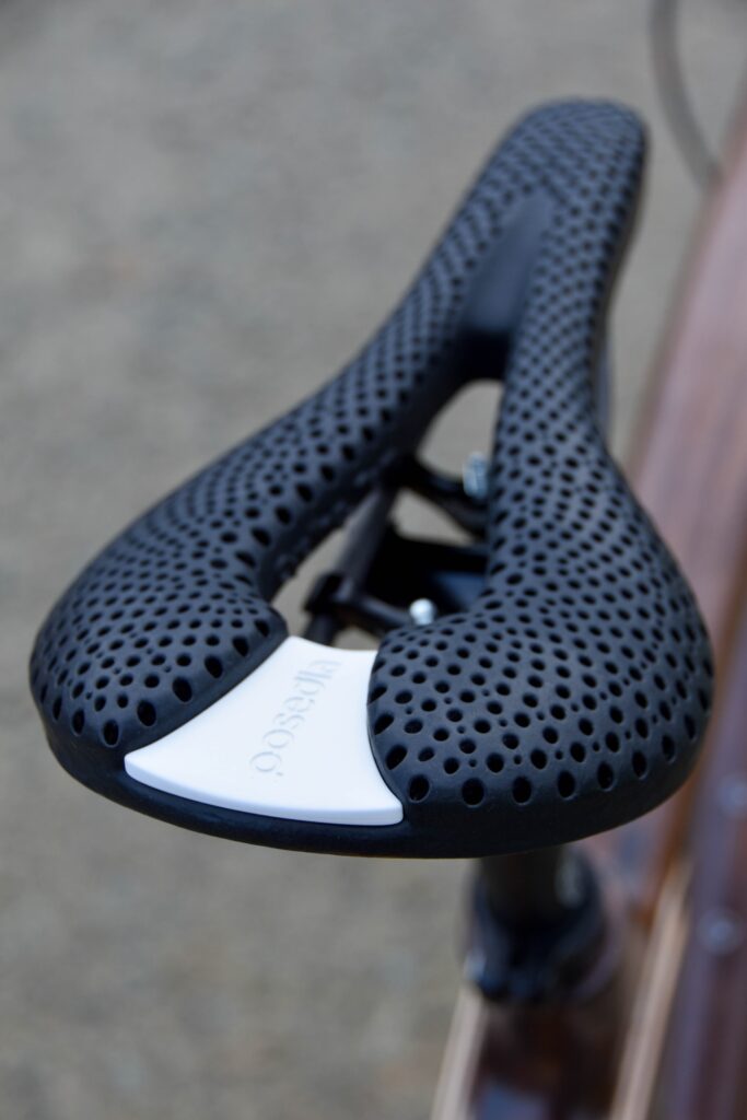 Posedla 3D printed saddle in black showing perforated lattice structure against wooden Zafi frame