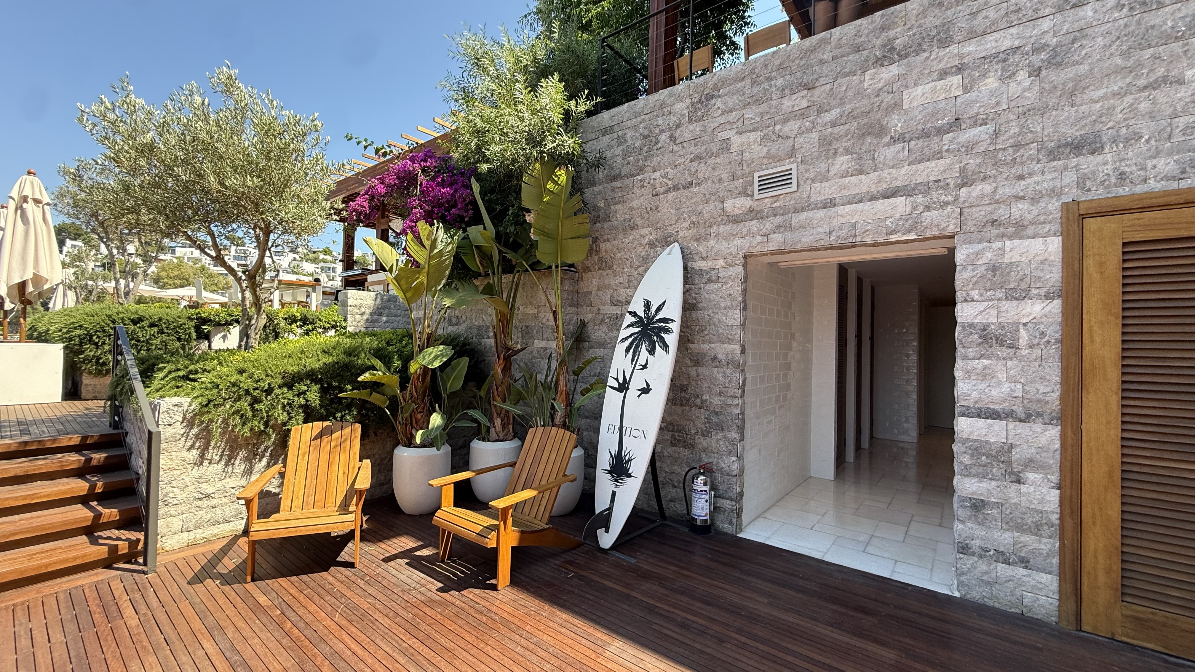 Beach club seating area — natural timber, surfboard and lush planting at the pier entrance