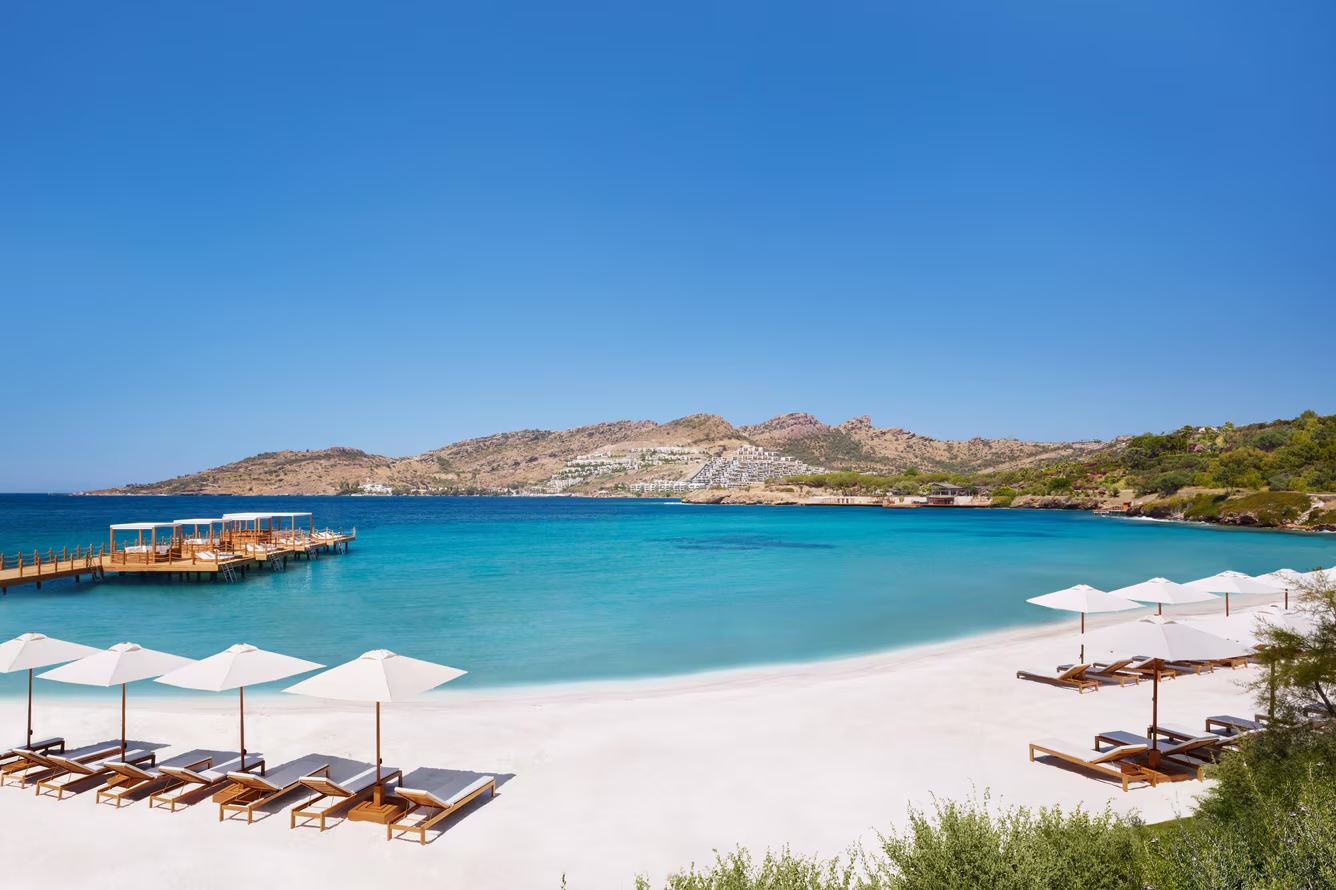 The private beach — white sand, overwater cabanas and Bodrum peninsula beyond