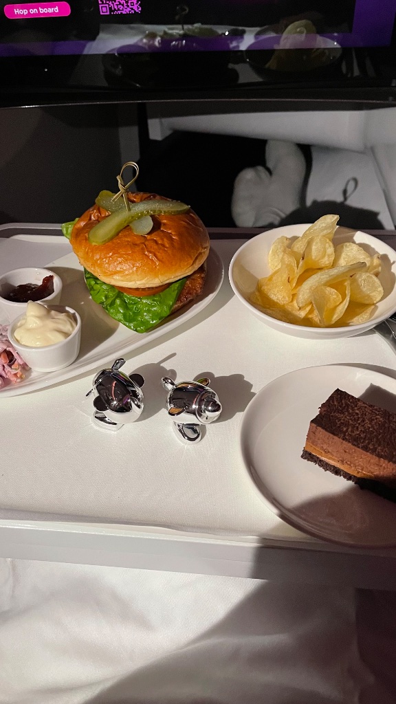 The flat bed made up — a proper duvet, full pillows, and a very opinionated travel companion